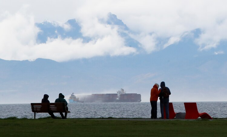La gente observa desde Clover Point Park cómo los remolcadores de rescate rocían agua sobre el buque portacontenedores Zim Kingston.