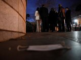 Un cubrebocas yace en el suelo junto a invitados que esperan para asistir a una fiesta, en Washington.