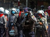 Un oficial de la policía antidisturbios dispara una bala de goma hacia los manifestantes