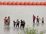 Migrantes caminan en frente de la barrera de boyas instaladas por el gobierno de Greg Abbott en imagen de archivo.