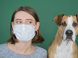 Una persona con cubrebocas posa junto a su perro.