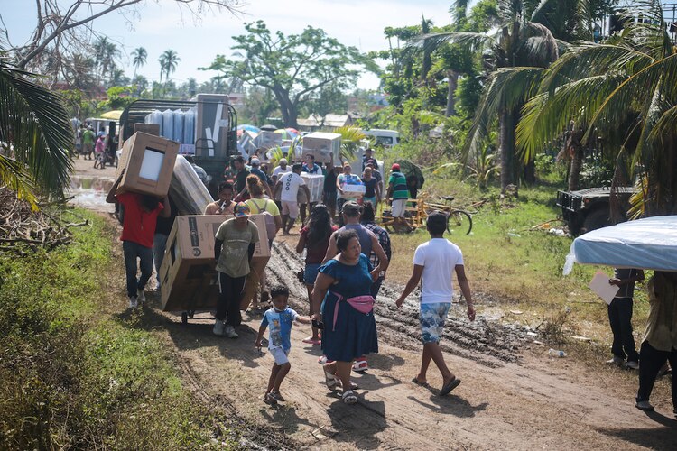 Habitantes de Llano Largo, Acapulco, caminan a sus hogares, tras recibir su paquete de enseres domésticos.
