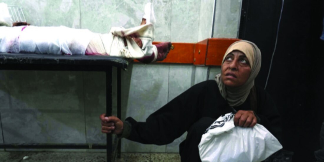 Mujer palestina espera junto a su hijo, herido al intentar acceder a alimentos, ayer.