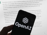 El logotipo de OpenAI se ve en un teléfono móvil frente a una pantalla de computadora que muestra el resultado de ChatGPT.