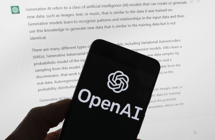 El logotipo de OpenAI se ve en un teléfono móvil frente a una pantalla de computadora que muestra el resultado de ChatGPT.