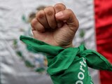 En la imagen una mujer posa con pañuelo verde símbolo del aborto legal, frente a una bandera de México durante el dictamen de la SCJN