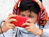 Un niño con audífonos se entretiene con un videojuego en un celular