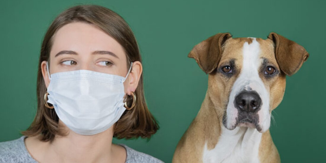 Una persona con cubrebocas posa junto a su perro.