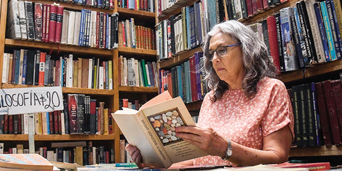 Mujer hojea un libro en una librería de Donceles, CDMX, en foto de archivo.