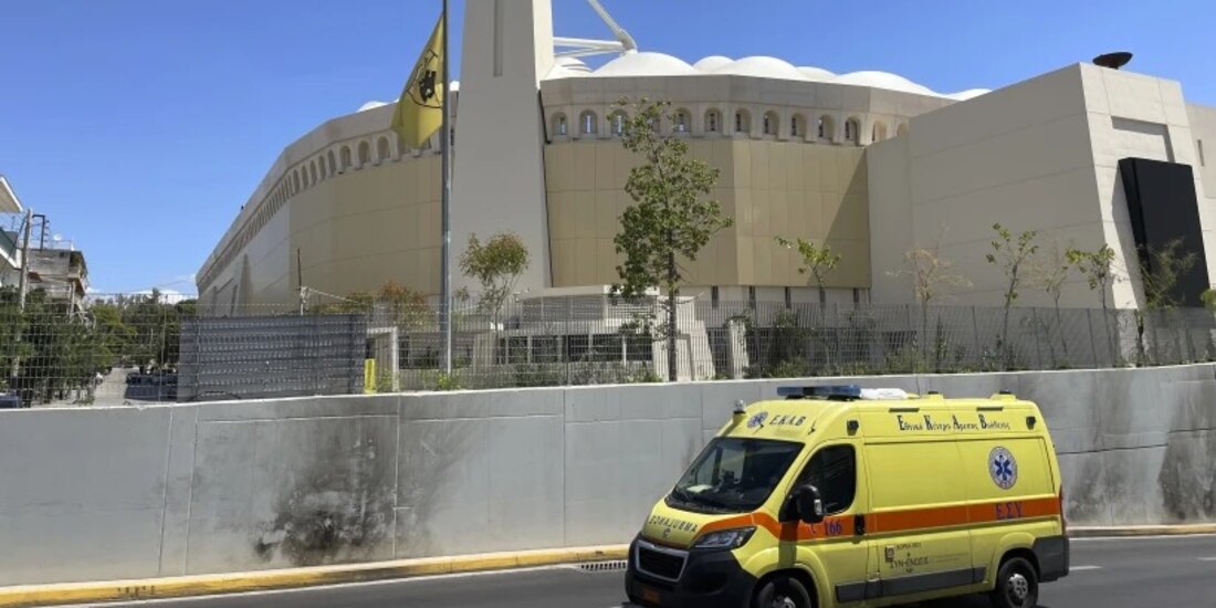 Una bandera del equipo de AEK de Atenas ondea a media asta ante el estadio OPAP mientras pasa una ambulancia, tras enfrentamientos durante la noche entre hinchas rivales en el suburbio de Nea Filadelfia, en Atenas, Grecia, el martes 8 de agosto de 2023.