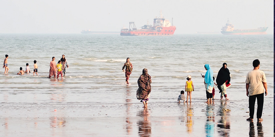 Personas disfrutan de la playa mientras buques mercantes permanecen anclados en el estrecho de Ormuz, Irán, ayer.