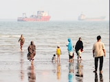 Personas disfrutan de la playa mientras buques mercantes permanecen anclados en el estrecho de Ormuz, Irán, ayer.