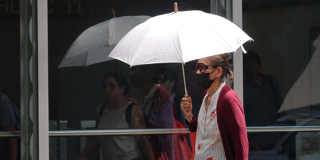 Una mujer usa cubrebocas y se cubre del sol en la primera ola de calor en mayo.