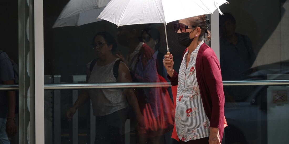 Una mujer usa cubrebocas y se cubre del sol en la primera ola de calor en mayo.