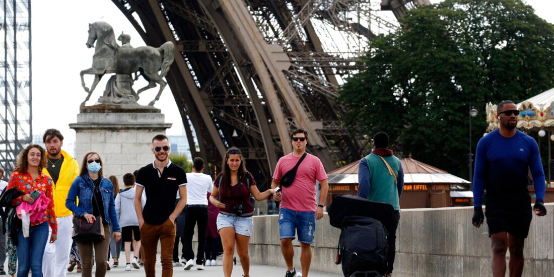Turistas camina al lado de la Torre Eiffel en París, este domingo 26 de julio.