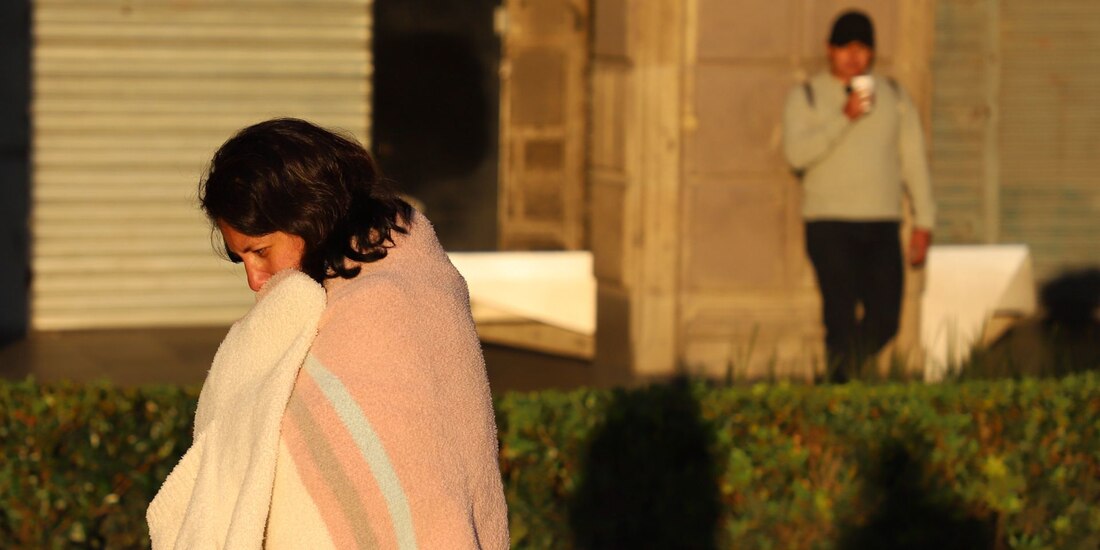Una persona busca mitigar el frío utilizando una cobija mientras camina por el Zócalo.