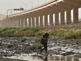 Mujer migrante que carga en hombros a su hijo cruza entre el Río Bravo, en la frontera en Juárez.