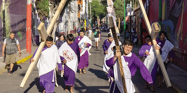 Algunas personas recorren las calles de Iztapalapa con una cruz.