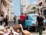 Hombres empujan un coche junto a un montón de basura en La Habana, ayer.
