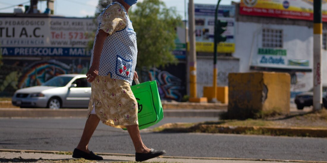 Una mujer adulta camina con cubrebocas y bolsa del mandado.