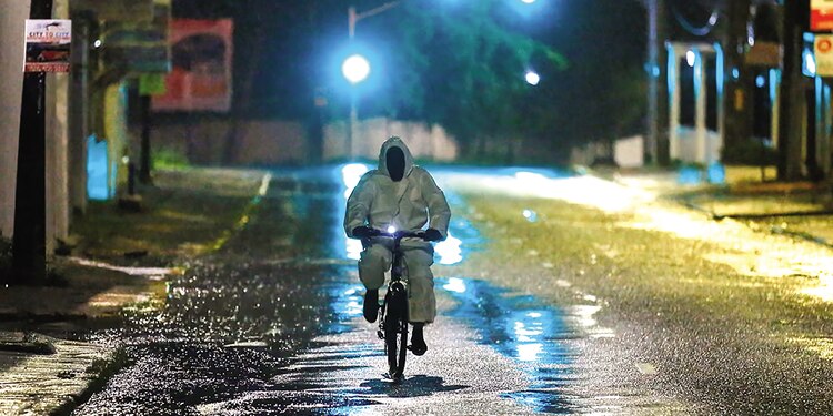 Un hombre con impermeable va en bicicleta por una calle de Kingston, ayer.