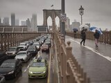 Personas con sombrillas caminan a un costado de los vehículos por el Puente de Brooklyn, luego de las fuertes lluvias del viernes 29 de septiembre de 2023, en Nueva York.