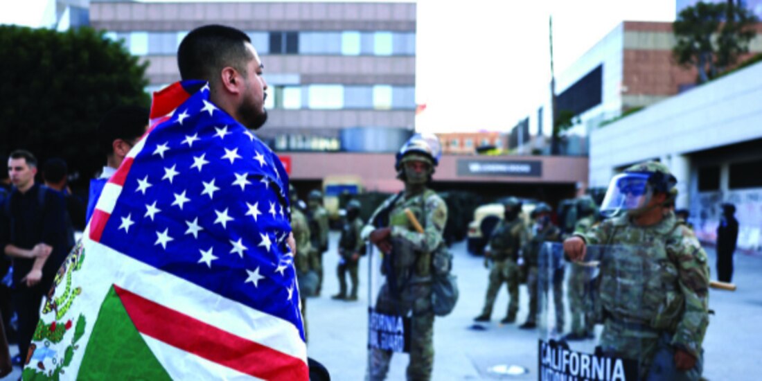 Un manifestante cubierto con la bandera mexicana y de EU frente a la Guardia Nacional de California, ayer.