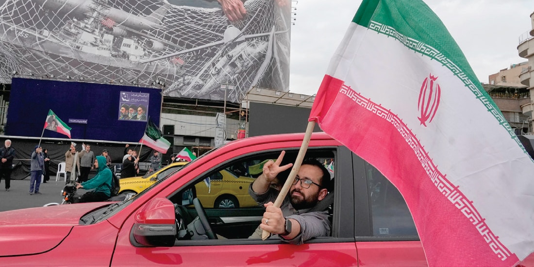 UN HOMBRE hace el signo de la victoria mientras porta una bandera iraní, el 13 de abril