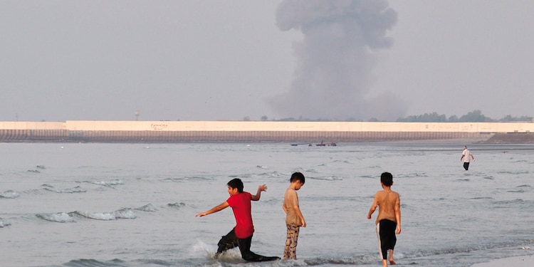 Tres niños juegan en Ormuz, mientras el humo se ve tras una explosión frente a Bandar Abbas, ayer.