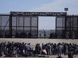Migrantes que cruzaron la frontera desde México hacia Estados Unidos esperan a un costado del muro fronterizo en donde agentes de la Patrulla Fronteriza de Estados Unidos montan guardia, el 30 de marzo de 2023, en una imagen tomada desde Cuidad Juárez, México. (AP Foto/Fernando Llano, Archivo)
