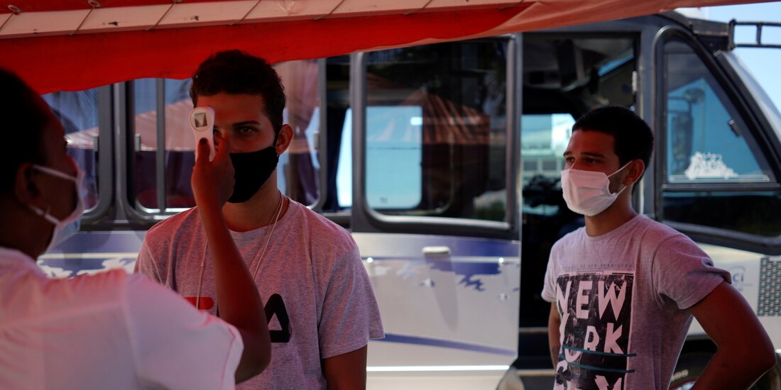 Un médico revisa la temperatura de dos hombres en La Habana.