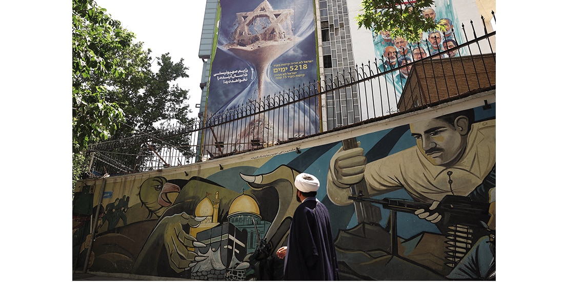 Un clérigo iraní camina junto a una valla publicitaria antiisraelí en un edificio en Teherán, antes de los ataques de EU, ayer.
