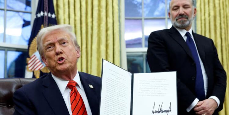 El presidente Trump sostiene una orden ejecutiva; al fondo, su secretario de Comercio Howard Lutnick, en fotografía de archivo.