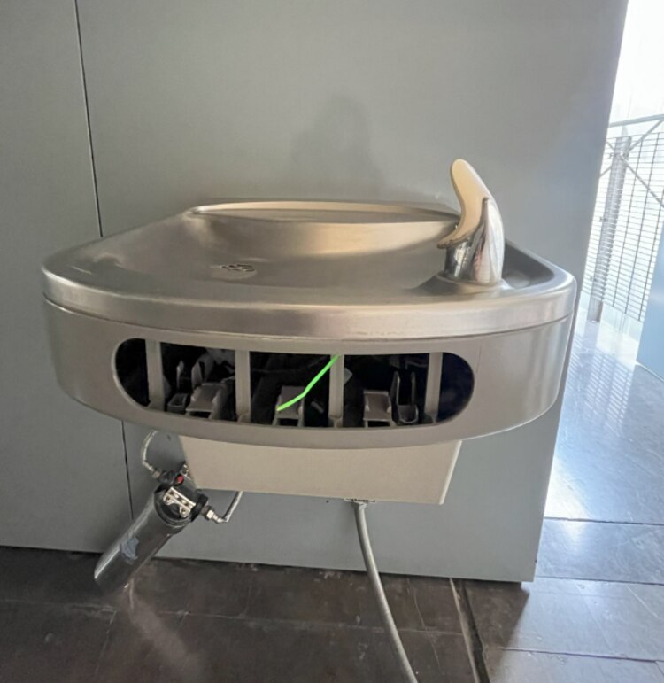 Un bebedero dañado y sin funcionar afuera de un baño de hombres.