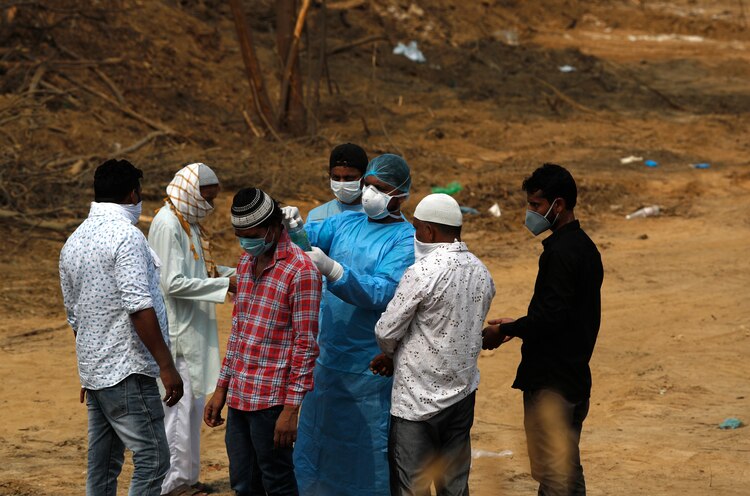 Familiares de una persona que murió por COVID-19 después de su entierro, en un cementerio en Nueva Delhi, India, el viernes 5 de junio de 2020.