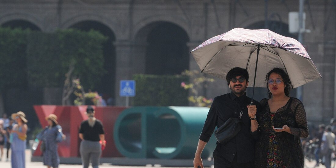 Una pareja camina por el Zócalo utilizando una sombrilla para cubrirse del sol.