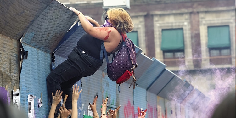 Una mujer trepa una de las bardas que protege Palacio Nacional.