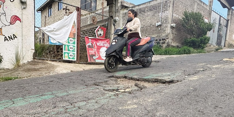 Una mujer esquiva con su motoneta un agujero en el pavimento.
