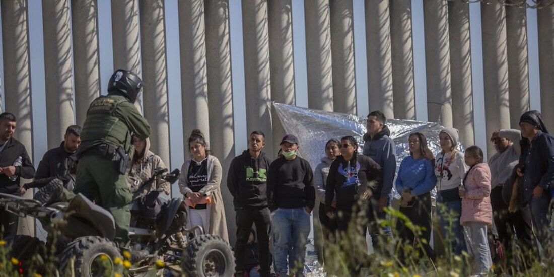 Un agente de EU habla con migrantes que cruzaron la frontera para pedir asilo, ayer.
