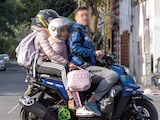 DOS ADULTOS, uno sin casco, viajan con una niña en una motoneta, el 31 de agosto
