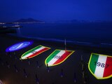El escudo del Napoli y tres "Scudettos" referentes a sus dos títulos anteriores y al que podría conseguir, se proyectan en la playa de Posillipo, el jueves 27 de abril de 2023 (Alessandro Garofalo/LaPresse via AP)