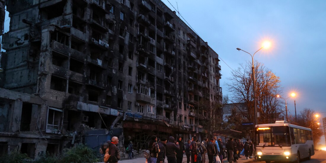 Ciudadanos esperan un autobús frente a un edificio dañado por los combates en Mariupol, Ucrania, ayer.