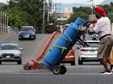 Un hombre transporta un tanque de gas con su diablito de carga por la calle