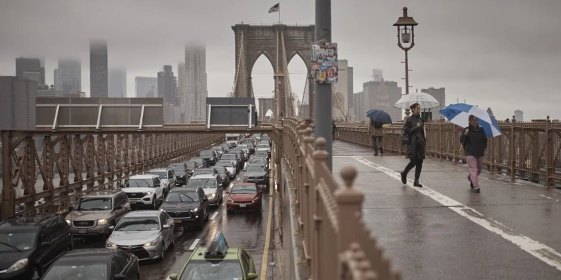 Personas con sombrillas caminan a un costado de los vehículos por el Puente de Brooklyn, luego de las fuertes lluvias del viernes 29 de septiembre de 2023, en Nueva York.