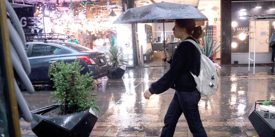 Una mujer se cubre de la lluvia con un paraguas, mientras camina por las calles de la Ciudad de México.