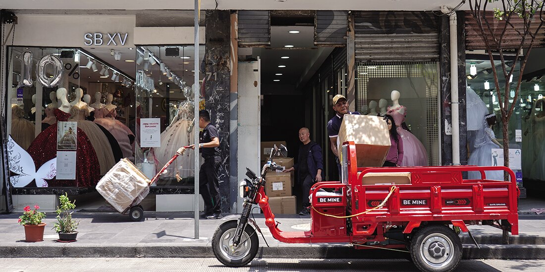 Trabajadores cargan un vehículo con cajas que sacan de un edificio, mientras un hombre con rasgos asiático los mira, el martes.