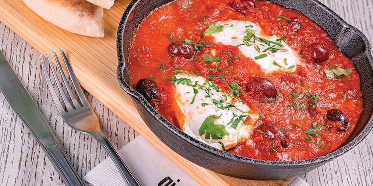 Shakshuka. Tres huevos pochados en salsa de jitomate, aceitunas y pimiento morrón. Con pan pita artesanal al lado.