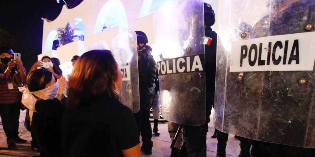 Mujeres protestan frente a policías luego de los actos de represión contra una movilización en Cancún.