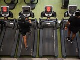 Miembros de un gimnasio corren dejando libre una caminadora entre ellos para mantener la sana distancia.