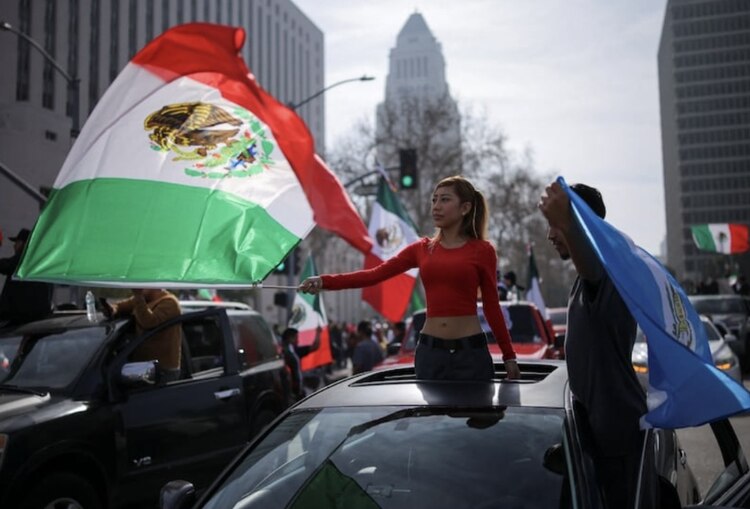 Una mujer abordo de un automóvil con la bandera de México en su mano